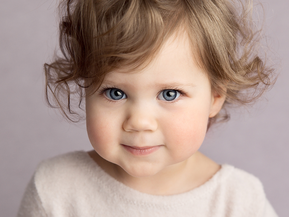 A studio portrait of a 1 year old girl with a slight smile
