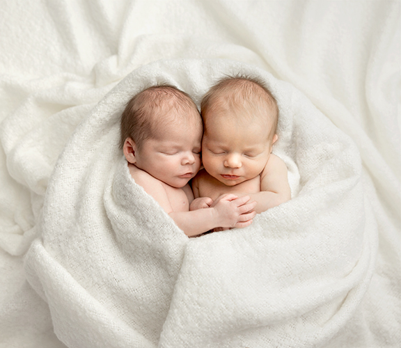 Twin newborns sleeping, wrapped up in white blanket