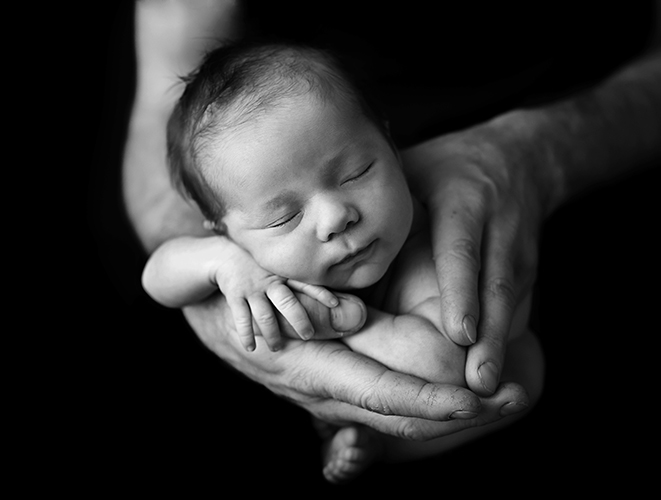 Black and white professional photo of newborn baby in dads hands