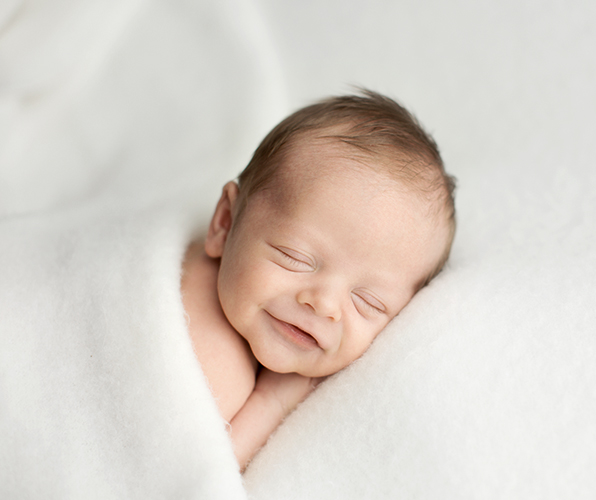 Professional newborn photo of sleeping baby smiling